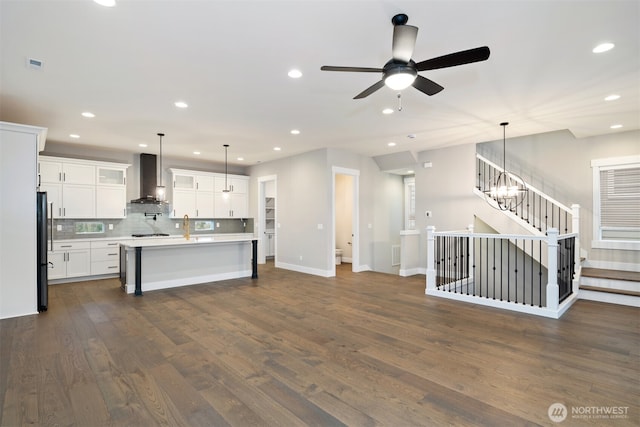 kitchen featuring dark wood-style flooring, freestanding refrigerator, a kitchen island with sink, ventilation hood, and light countertops