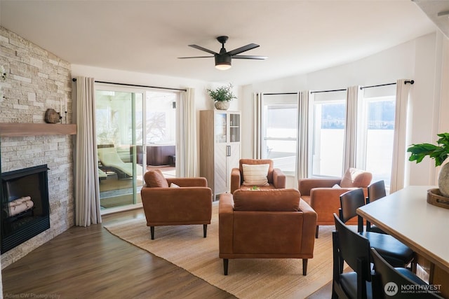 living area with lofted ceiling, a stone fireplace, wood finished floors, and a ceiling fan