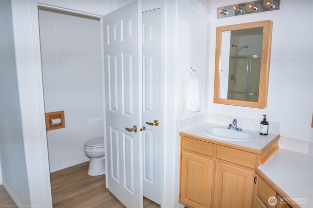 bathroom with toilet, an enclosed shower, wood finished floors, and vanity