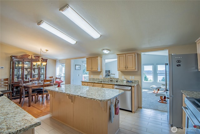 kitchen featuring stainless steel appliances, a healthy amount of sunlight, light brown cabinets, a kitchen island, and a sink