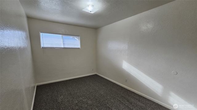 empty room featuring a textured ceiling, a textured wall, dark carpet, and baseboards