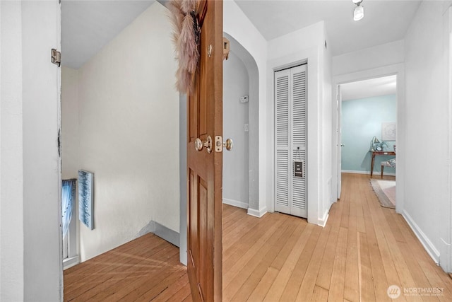 hall with baseboards, arched walkways, and light wood finished floors