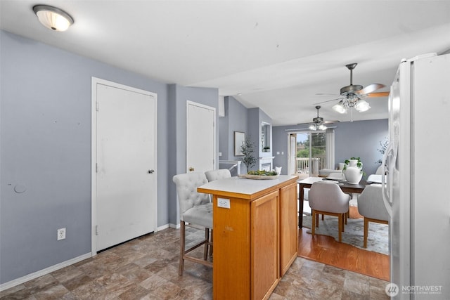 kitchen with a kitchen breakfast bar, a kitchen island, freestanding refrigerator, baseboards, and vaulted ceiling