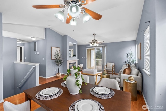 dining room featuring baseboards, lofted ceiling, wood finished floors, and a tiled fireplace