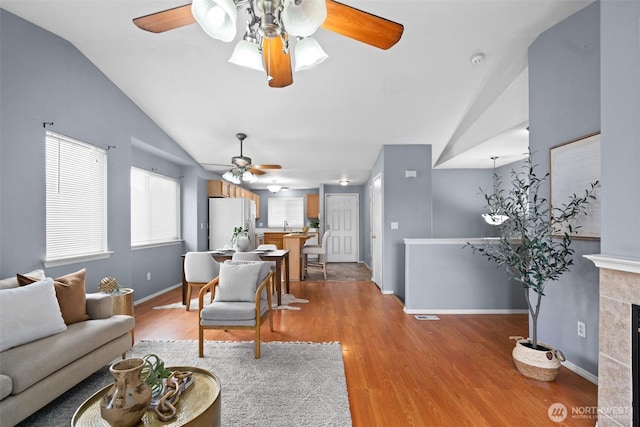 living area featuring a tiled fireplace, vaulted ceiling, light wood finished floors, and ceiling fan