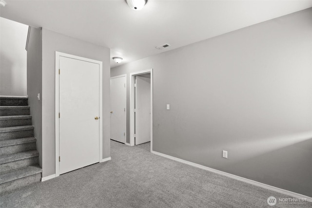 carpeted spare room featuring stairway, baseboards, and visible vents