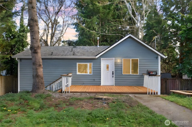 view of front of home featuring a shingled roof, fence, and a deck