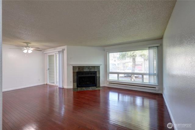 unfurnished living room featuring baseboards, dark wood finished floors, a tile fireplace, a textured ceiling, and a baseboard heating unit