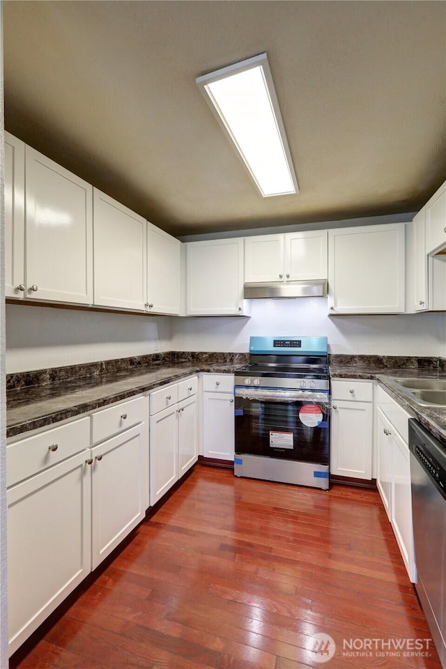 kitchen featuring under cabinet range hood, a sink, white cabinetry, appliances with stainless steel finishes, and dark wood-style floors