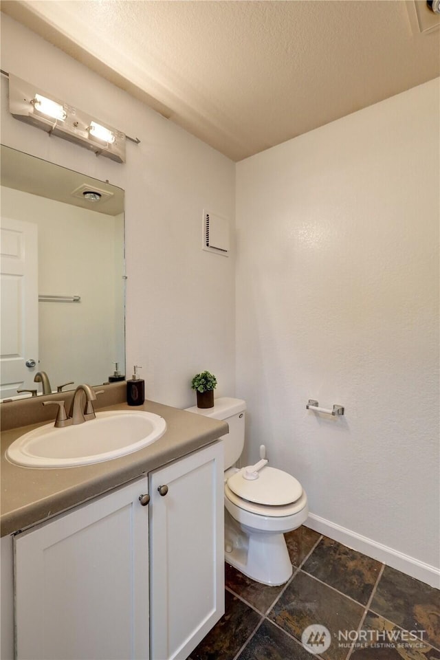 half bath featuring a textured ceiling, toilet, visible vents, vanity, and baseboards