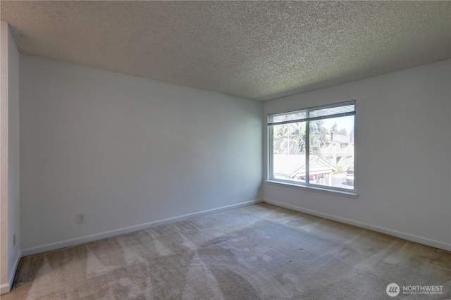 carpeted empty room featuring a textured ceiling and baseboards