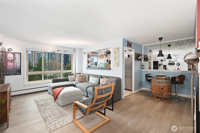 living area with baseboard heating, a textured ceiling, baseboards, and wood finished floors