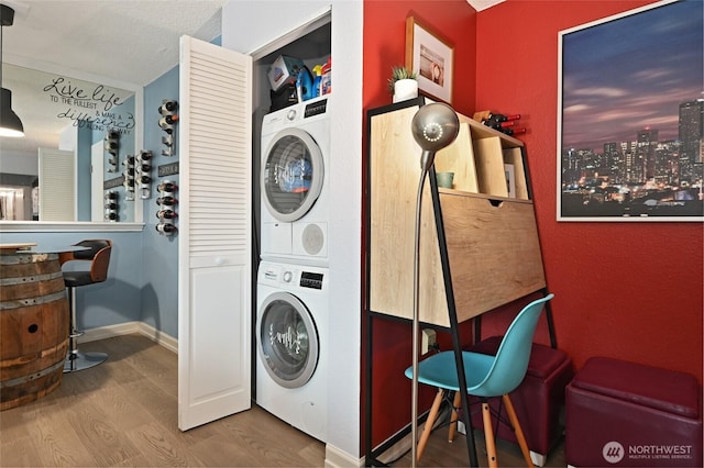 clothes washing area featuring laundry area, wood finished floors, stacked washer and clothes dryer, and baseboards