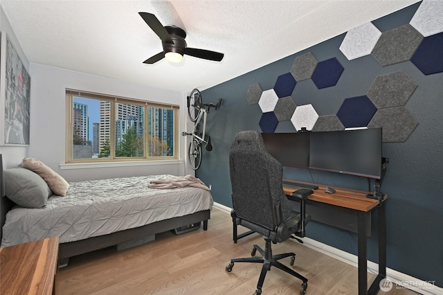 bedroom featuring a ceiling fan, an accent wall, baseboards, and wood finished floors