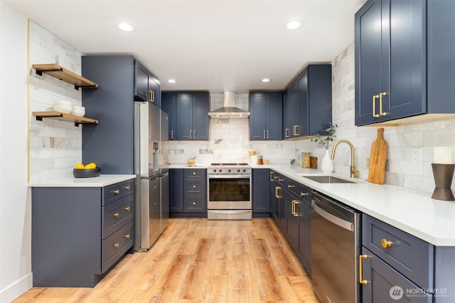 kitchen with open shelves, light wood-style flooring, appliances with stainless steel finishes, a sink, and wall chimney range hood