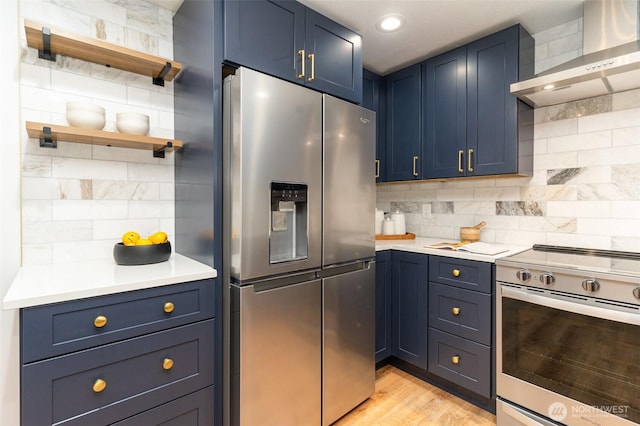 kitchen featuring light countertops, appliances with stainless steel finishes, wall chimney range hood, and blue cabinets