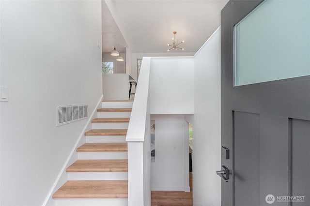 stairway with baseboards, visible vents, wood finished floors, a high ceiling, and a notable chandelier