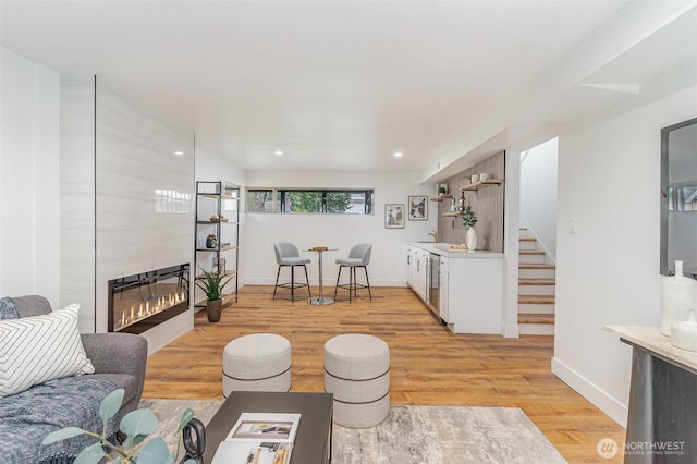 living room featuring light wood finished floors, baseboards, stairs, a fireplace, and recessed lighting