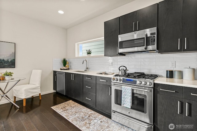 kitchen featuring light countertops, appliances with stainless steel finishes, a sink, and dark cabinetry