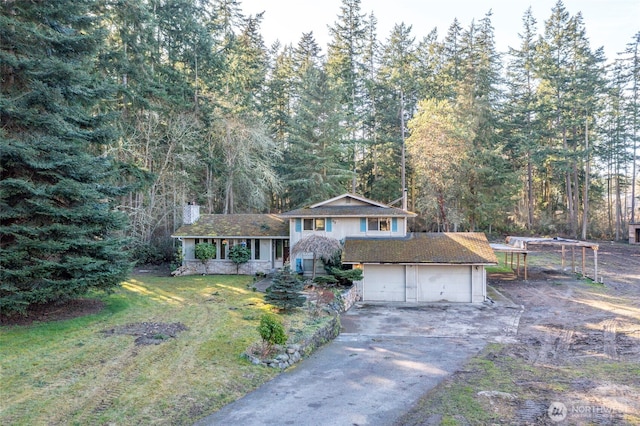 split level home with a garage, a forest view, driveway, and a front lawn