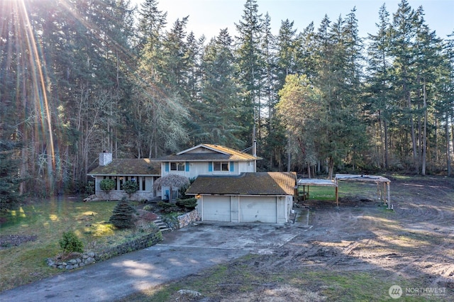 view of front of property featuring a garage, driveway, and a view of trees