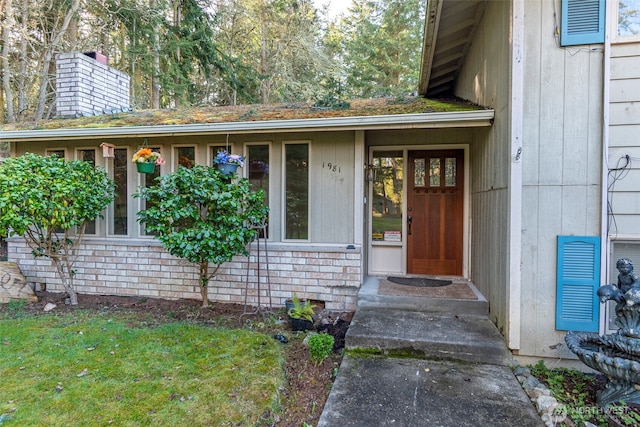 doorway to property featuring brick siding, a chimney, and visible vents