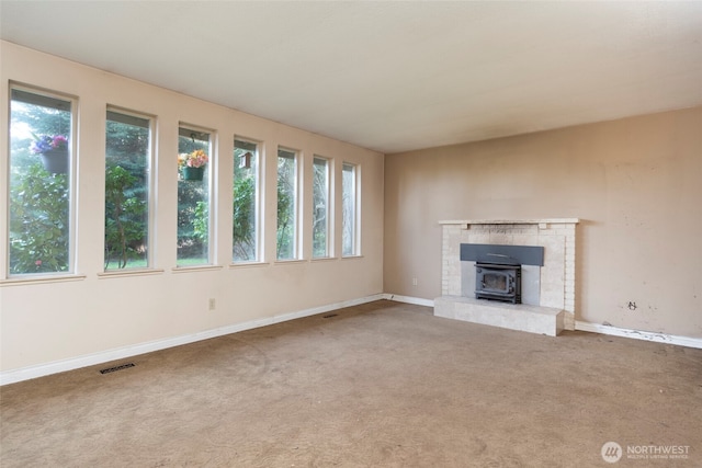 unfurnished living room featuring a wood stove, a wealth of natural light, carpet, and visible vents