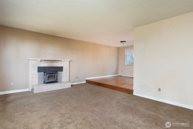 unfurnished living room featuring carpet floors, a wood stove, and baseboards