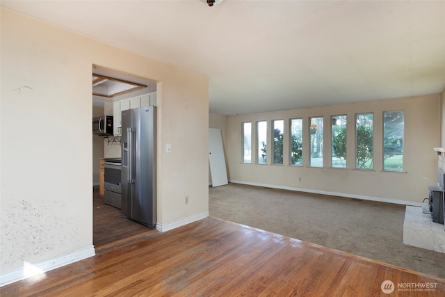 empty room featuring a wood stove, baseboards, and wood finished floors