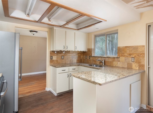 kitchen with dark wood-style flooring, freestanding refrigerator, white cabinets, a sink, and a peninsula