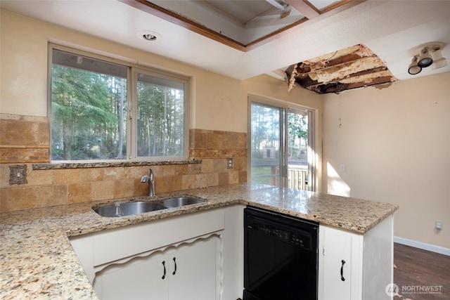 kitchen with a peninsula, a sink, white cabinets, black dishwasher, and light stone countertops