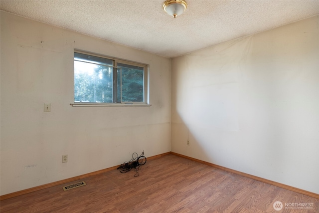 spare room featuring visible vents, a textured ceiling, baseboards, and wood finished floors