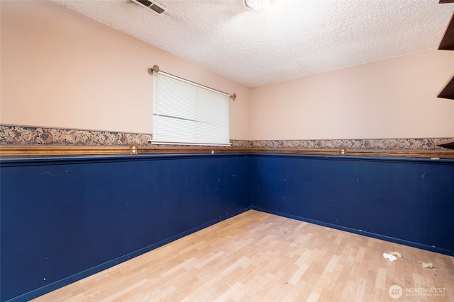 empty room featuring a textured ceiling, a wainscoted wall, wood finished floors, and visible vents