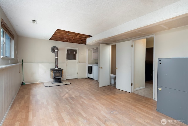 unfurnished living room with a wood stove, light wood-style flooring, visible vents, and washing machine and clothes dryer