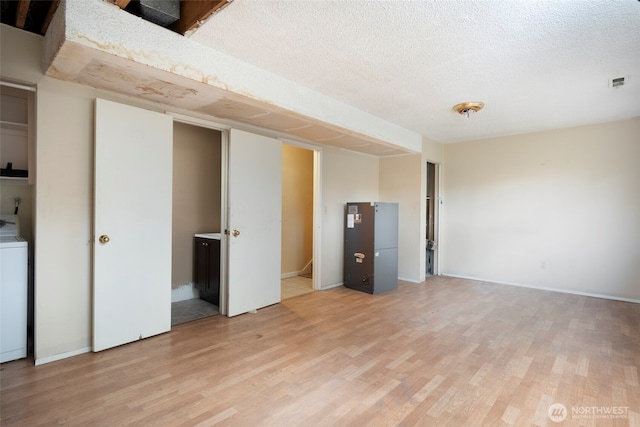 interior space featuring a textured ceiling, visible vents, baseboards, light wood-style floors, and washer / clothes dryer