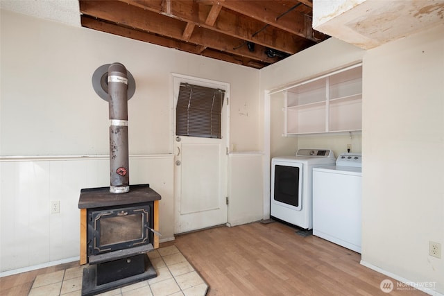 washroom featuring laundry area, a wainscoted wall, a wood stove, light wood-style floors, and washing machine and dryer