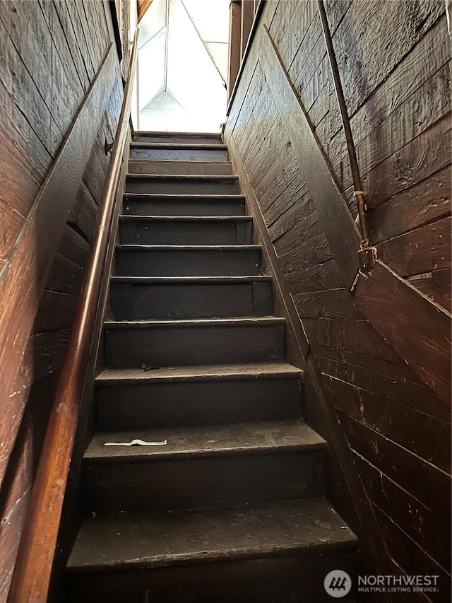 stairway featuring wooden walls