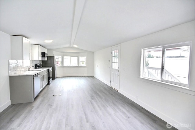 kitchen featuring baseboards, vaulted ceiling with beams, stainless steel appliances, light countertops, and light wood-style floors