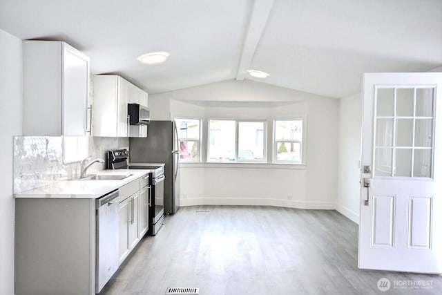 kitchen featuring vaulted ceiling with beams, light wood finished floors, stainless steel appliances, light countertops, and a sink