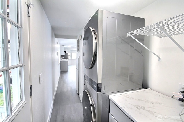 laundry area featuring stacked washer / drying machine, laundry area, baseboards, and wood finished floors