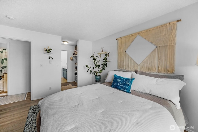 bedroom featuring a spacious closet, wood finished floors, a closet, and baseboards