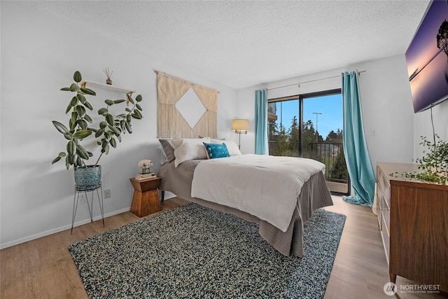 bedroom featuring baseboards, a textured ceiling, wood finished floors, and access to outside