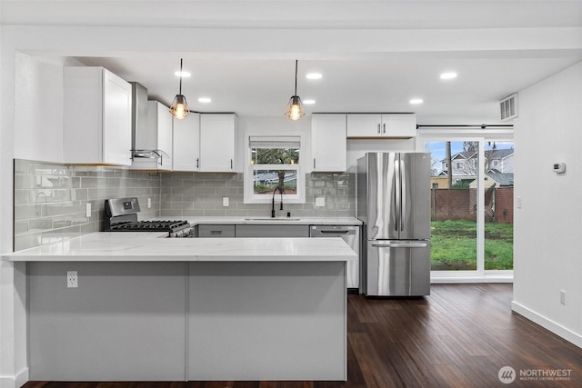 kitchen featuring visible vents, a peninsula, stainless steel appliances, wall chimney range hood, and a sink