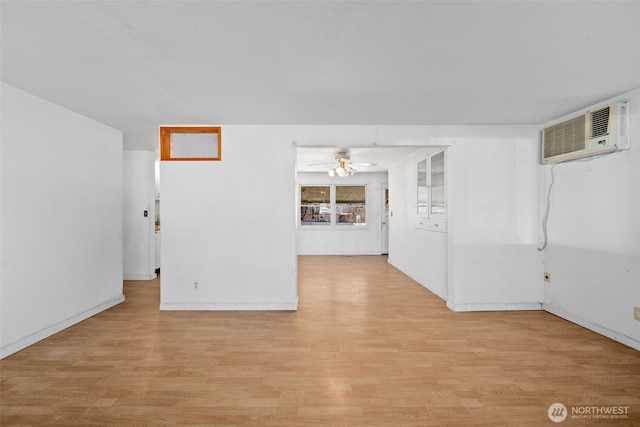 spare room with baseboards, a wall unit AC, light wood-style flooring, and a ceiling fan