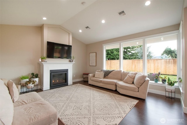 living area with visible vents, vaulted ceiling, dark wood-type flooring, and a glass covered fireplace