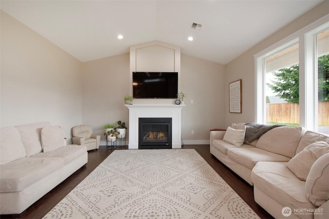 living area featuring dark wood-style floors, visible vents, vaulted ceiling, and a glass covered fireplace