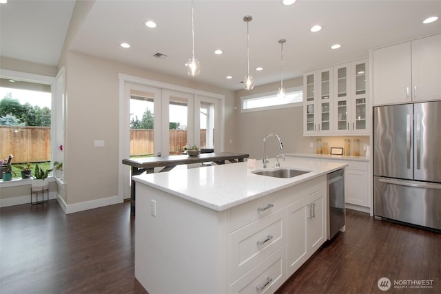 kitchen featuring stainless steel appliances, a sink, a center island with sink, dark wood-style floors, and glass insert cabinets