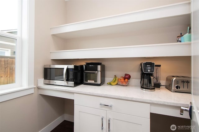 kitchen with white cabinetry, stainless steel microwave, open shelves, and built in study area