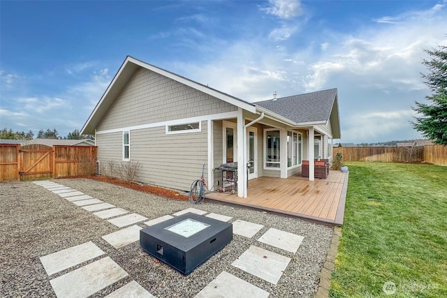 back of property featuring a lawn, an outdoor fire pit, a gate, a deck, and a fenced backyard