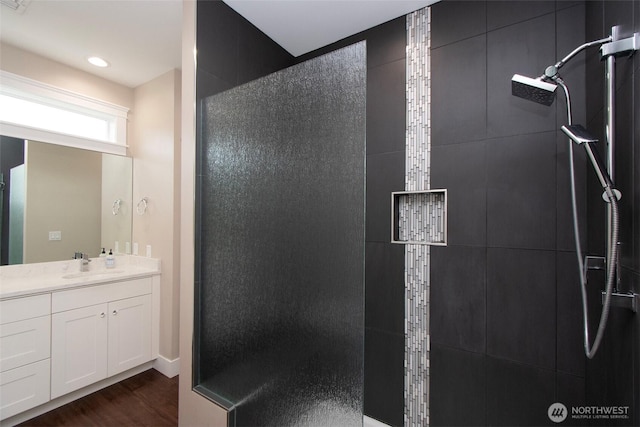 full bathroom featuring recessed lighting, a tile shower, vanity, and wood finished floors